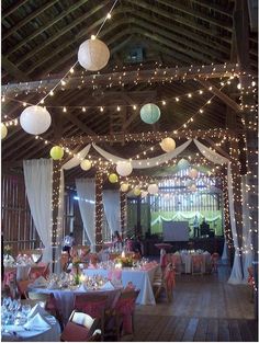 the inside of a barn decorated with lights and paper lanterns