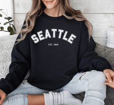 Experience the essence of the West Coast with our Seattle Sweatshirt! Perfect as a gift or souvenir, this long-sleeve shirt captures the spirit of Seattle, Washington. Embrace the vibe of the city in comfort and style. It's a great addition to your collection, showcasing your love for the Emerald City and the beautiful state of Washington. Celebrate the uniqueness of Seattle and the Pacific Northwest with this cozy crewneck! Features Include: Medium-heavy fabric blend (50% cotton and 50% polyester), perfect for the colder months A classic fit paired with a crew neckline makes this sweatshirt extremely cozy and perfect for all occasions Durable and designed to maintain its shape wash after wash Tear away label Runs true to size No side seams for comfort and appearance  Made using 100% ethic Long Sleeve Sweatshirt With Lettering As Gift, Long Sleeve Pre-shrunk T-shirt As Gift, Pre-shrunk Long Sleeve T-shirt As A Gift, Long Sleeve School Spirit T-shirt With Lettering, Long Sleeve T-shirt With School Spirit Lettering, Long Sleeve Letter Print Sweatshirt Gift, Long Sleeve Sweatshirt With Letter Print As Gift, Long Sleeve Letter Print Sweatshirt For Gift, Casual Long Sleeve T-shirt As Gift