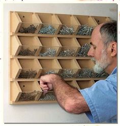 an older man is looking at screws in a box on the wall and holding them up