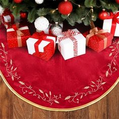 a christmas tree with presents under it on a red tablecloth and wooden flooring