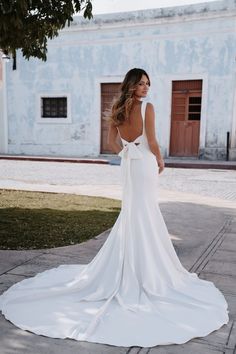 a woman in a white wedding dress is standing on the sidewalk and looking back at the camera