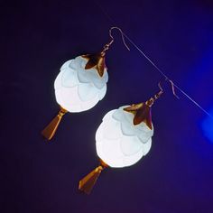 two white lamps hanging from strings on a dark blue background, one is shaped like a flower and the other is shaped like a bird