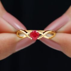 a woman's hand holding a gold ring with a red stone in the middle