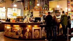 people standing in line at the counter of a coffee shop with menus on the wall