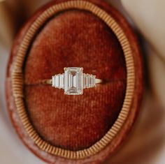 an emerald cut diamond ring sits in a velvet case on top of a wooden surface