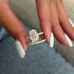 a woman's hand with white nails and two rings on her fingers, holding a diamond ring