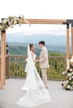 a bride and groom standing in front of a gazebo with mountains in the background