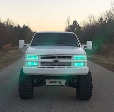 a white truck parked on the side of a road with its lights on and it's front bumper up