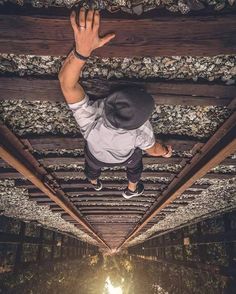 a man standing on top of a wooden bridge under a skylight with his hands in the air