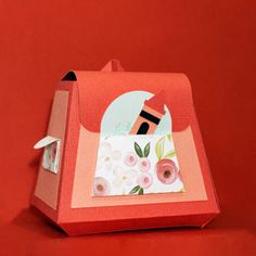 an origami box with a paper doll in it on a red table top