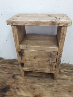 a small wooden cabinet sitting on top of a hard wood floor next to a white wall