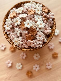 small crocheted flowers in a basket on a wooden table next to scattered petals