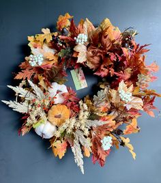 a wreath made out of leaves and pumpkins on a gray surface with a tag