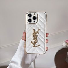 a person holding up a white phone case with a gold saint laurent logo on it