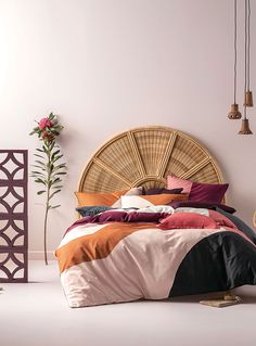 a bed with colorful sheets and pillows in a white room next to a wicker headboard