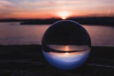 a glass ball sitting on top of a rock next to the ocean at sunset or dawn