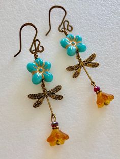 "Adorable turquoise blue Czech glass puffed daisies with topaz yellow bellflowers and vintage bronze stamped dragonfly charms. Matte turquoise 14 mm Czech glass puffy 5 petal flowers are etched with metallic gold and wire wrapped in vintage bronze with 6 x 9 mm translucent topaz yellow bellflowers accented with tiny burnt orange crystals. Lightweight dangles hang on handmade and hammered vintage bronze ear wires. Total drop length is 2 1/2\"." Vintage Turquoise Flower Earrings, Vintage Turquoise Dangle Flower Earrings, Turquoise Flower Charm Earrings For Gift, Turquoise Flower Earrings As A Gift, Gift Turquoise Flower Charm Earrings, Gift Turquoise Flower Earrings, Nickel Free Turquoise Flower Earrings, Turquoise Nickel Free Flower Earrings, Turquoise Dangle Earrings With Flower Charm