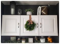 a wreath is hanging on the front of white cupboards with candles and other items