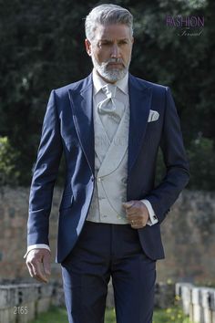 a man in a blue suit and white shirt is walking down the street with his hands in his pockets