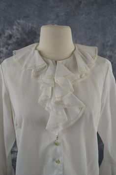 1960's/1970's White Ruffled, Three Quarter Sleeve Blouse White blouse with a round collar and a ruffled front and sleeves, the sleeves are three quarters in length. There are two hidden buttons behind the ruffled front and the majority of the buttons start below the bust. Label: A Jane Holly Inc Original 100% Dacron Polyester Measurements are taken flat; Shoulders: 15 1/2 inches Sleeve: 18 inches Cuff: 5 inches Neck: 7 inhces Bust: 20 1/2 inches Waist: 19 inches Length (shoulder to hem): 21 1/4 Three Quarter Sleeve Blouses With Collar Bulotus Top, Quarter Sleeve Blouse, Three Quarter Sleeve Blouses, Cadiz, Blouse White, White Blouse, Three Quarter Sleeves, Quarter Sleeve, Round Collar