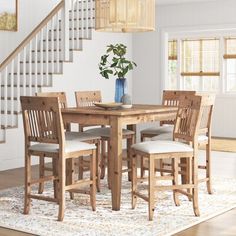 a dining room table and chairs in front of a stair case with white carpeting