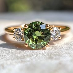 a green ring sitting on top of a white stone surface with three diamonds around it