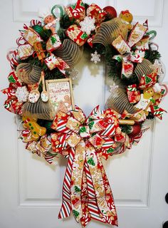 a christmas wreath with candy canes and decorations on the front door, hanging from a white door