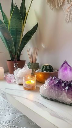 candles and crystals on a white mantle in front of a potted plant with green leaves