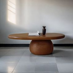 a wooden table sitting on top of a white floor next to a vase and book