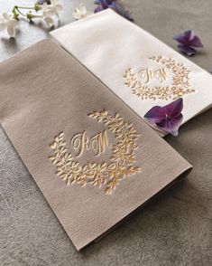 two napkins with embroidered monogrammed designs on them, one is gold and the other is white