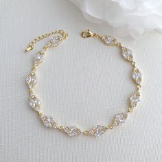 a gold bracelet with crystal stones on it and a white flower in the back ground