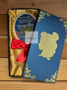 a blue and gold box with a red ribbon around it that has a card in it