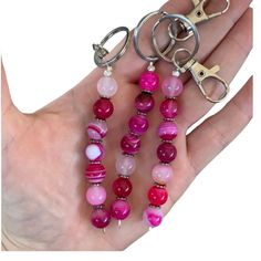 a woman's hand holding three pairs of pink and red beaded key chains