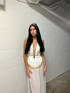 a woman standing in front of a brick wall wearing a white dress with gold trim