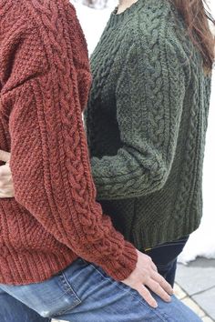 two people standing next to each other with their hands on their hipss, wearing sweaters and jeans