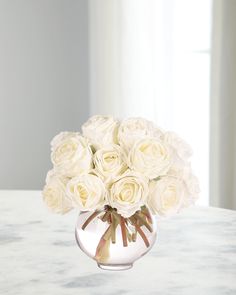 a vase filled with white roses sitting on top of a marble table next to a window