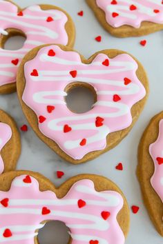 heart shaped donuts with pink frosting and sprinkles arranged on a table