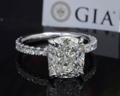 a cushion cut diamond ring sitting on top of a black table with a sign in the background