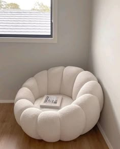 a white chair sitting in front of a window next to a book on top of a wooden floor