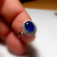 a close up of a person's hand holding a ring with a blue stone