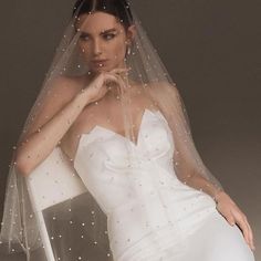 a woman wearing a white wedding dress with a veil on her head and one hand under her chin