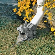 an animal statue laying on the ground next to yellow flowers and a white fence post