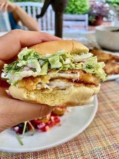 a person is holding up a sandwich with lettuce and chicken on it in their hand