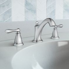 a bathroom sink with two faucets and marble wall tiles in the back ground