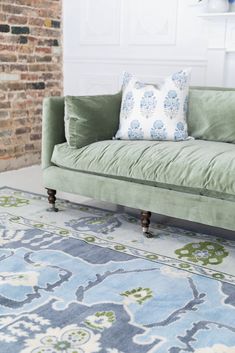 a green couch sitting on top of a blue rug next to a white brick wall