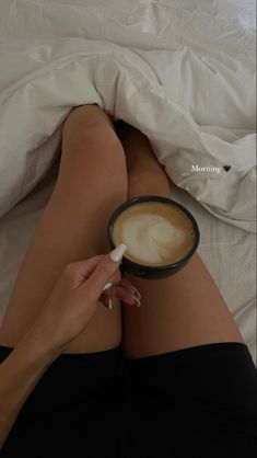 a woman laying in bed with her legs crossed holding a cup of coffee and spoon