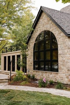 a stone house with large arched windows in the front yard