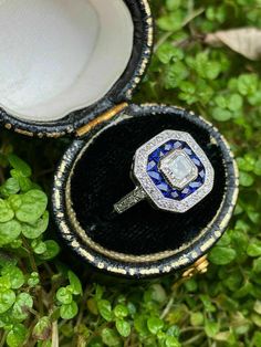 an open ring box with a diamond and blue glass in it sitting on some grass