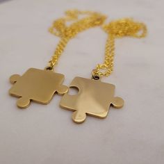 two pieces of gold puzzle necklaces on a white surface with one piece missing from the other