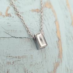 a silver necklace with a rectangle pendant hanging from it's side on a wooden surface